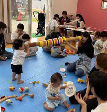 長い筒の中をスタッフと向かい合わせでのぞき込み，楽しむ子ども。