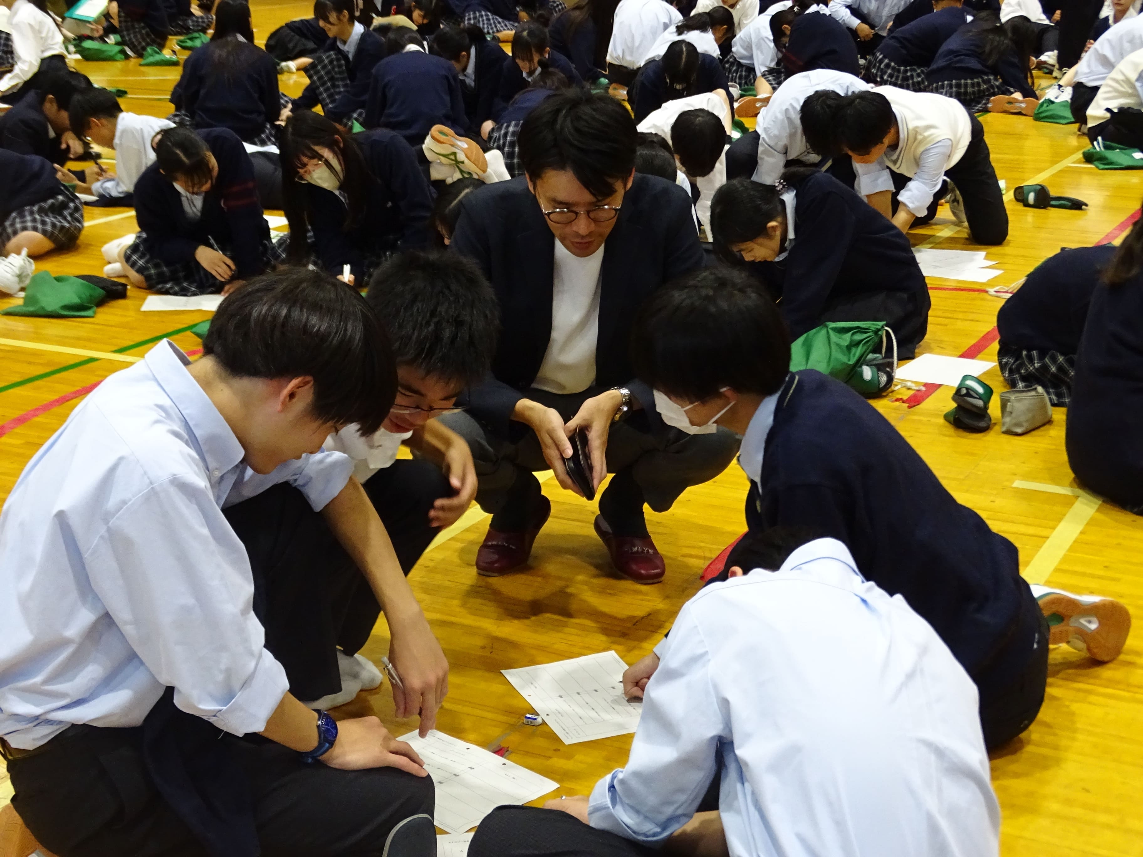 体育館の中で複数の中学生が一つの用紙を見つめている様子