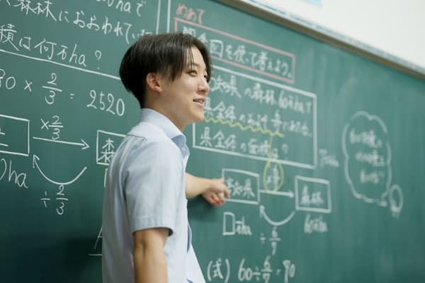 黒板の前で指をさす小学校教諭の写真