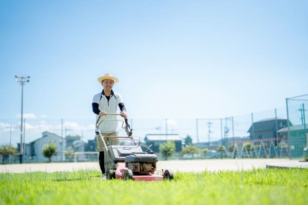 草刈り機を使用して草刈りを行う用務員の写真